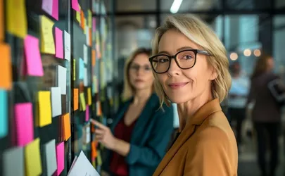 Eine Businessfrau steht vor einem Kanban Board und lächelt in die Kamera