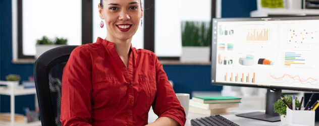 eine Frau in rotem Hemd sitzt am Schreibtisch mit Desktop-Computer